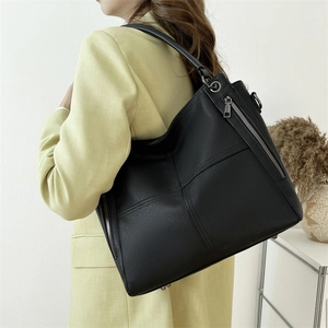 Black pebbled leather tote bag with side zippers worn by a model in a minimalist setting