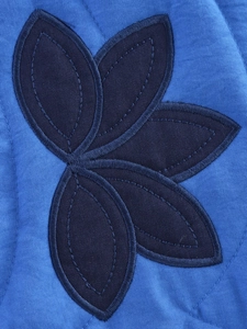Detailed view of dark blue leaf applique embroidery and quilted texture on cotton jacket
