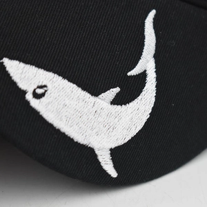 Detailed close-up of white shark embroidery on black washed cotton baseball cap fabric