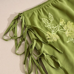 Detailed view of olive green fabric featuring yellow sequin flowers and side lace-up ties