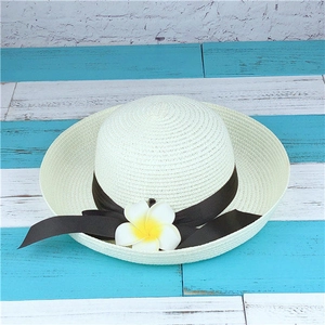 Detail of a straw sun hat featuring a brown ribbon and a white plumeria flower accent