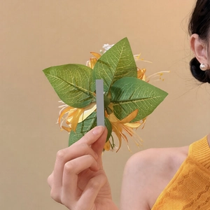 Detail of fabric flower hair clip with orange petals and textured green leaves