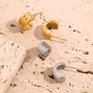 Close-up of triple-layered C-shaped earrings in gold and silver finish on stone