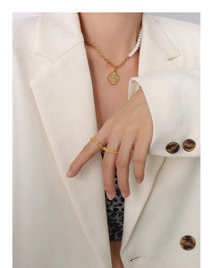 Détail d'un collier pendentif pièce dorée et perles porté avec un costume blanc