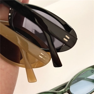 Detail of oval sunglasses with metallic rivet accents in black, amber, and marble green