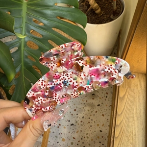 Close-up of a large mosaic acetate hair claw clip held by hand in a natural outdoor setting