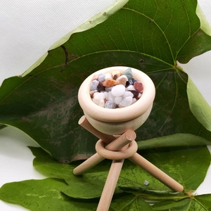 Macro view of a natural wooden tripod bowl filled with multicolored pebbles and green leaves