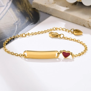 Détail macro du bracelet en acier doré avec barre à graver et breloque cœur rouge vif