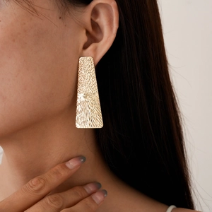 Detail of long golden geometric trapezoid earrings with textured sunburst pattern