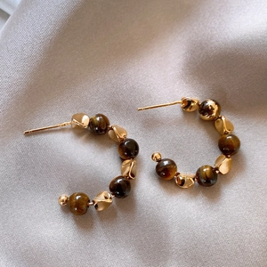 Macro view of 18K gold plated C-shaped earrings with tiger eye beads on grey silk