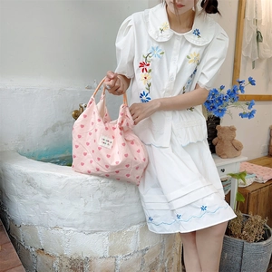 Detail of pink heart-print canvas tote bag with embroidered label held by female model