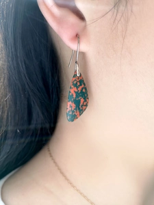 Detailed close-up of water drop turquoise earrings with red and green spots on model