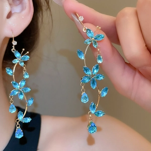Detail of long tassel earrings with blue flower and butterfly pendant on model