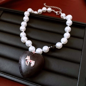 Detail of vintage heart stone pendant with silver horse logo on pearl bead necklace