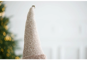 Close-up of a cozy beige knitted Christmas gnome hat with soft festive bokeh lights