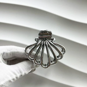 Detailed view of silver metallic scallop shell hair claw clip held by a gloved hand