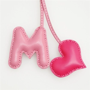 Close-up of leather letter M and heart charm with fine stitching and pink hues