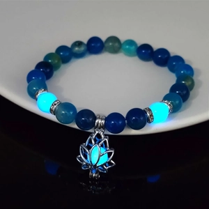 Detailed view of luminous lotus flower charm bracelet with teal beads in darkness
