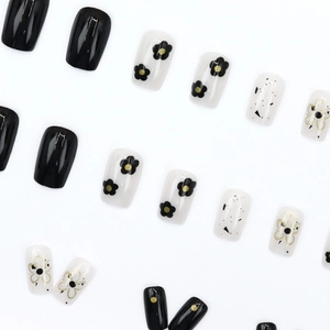 Minimalist black and white floral press-on nails with abstract gold accents on white background