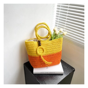Detail of woven straw tote bag with bicolor contrast and decorative wooden bead tassels