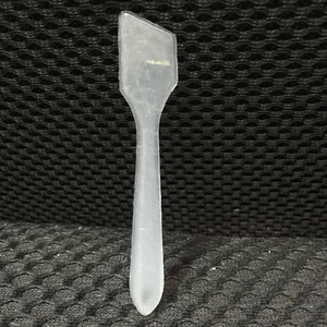 Macro view of a matte translucent plastic cosmetic spatula on a textured mesh surface