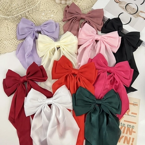 Flat lay of colorful oversized satin hair bow clips with long ribbons and smooth texture