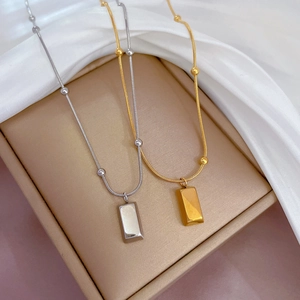 Detail shot of silver and gold rectangular bar pendants on beaded chains on silk