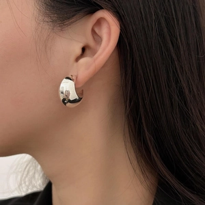 Close-up of a chunky silver C-shape stud earring on a model showing modern metal texture