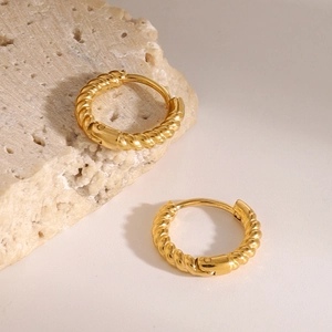 Detail view of gold twisted cable hoop earrings on a textured stone prop background
