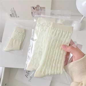 Close-up of cream white mesh socks with heart patterns in minimalist packaging