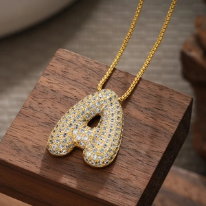 Detailed close-up of 18K gold plated letter A pendant with sparkling zircon on a wood block