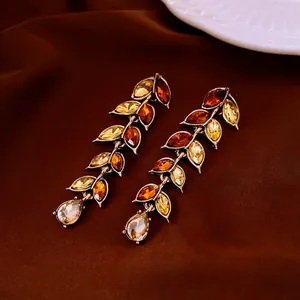 Vintage gold ear dangles with amber gems and leaf tassels on a luxury silk background