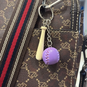 Detailed view of mini wooden baseball bat and purple leather ball keychain on a handbag