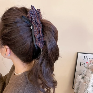 Close-up of a red checkered hair tie and black ribbon bow hair clip on a ponytail