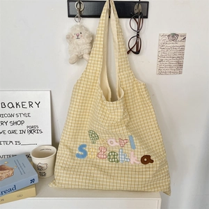 Close-up of yellow plaid tote bag featuring colorful letter embroidery on a white wall