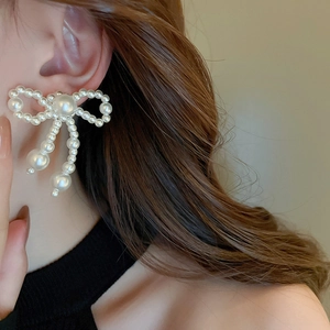 Close-up of elegant white faux pearl bow earrings on model showing tassels and bow detail