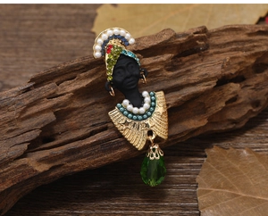 Detailed shot of ethnic tribal brooch with pearls and green teardrop gem on vintage wood