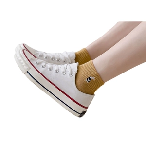 Yellow cotton socks with small embroidery shown on feet with white canvas sneakers