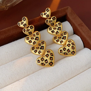 Close-up of golden leopard print heart earrings resting in a beige velvet jewelry box