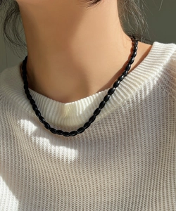 Close-up of minimalist black oval bead necklace worn over a white knitted sweater
