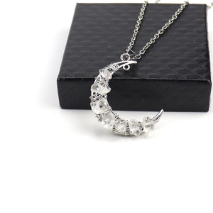 Close-up of crescent moon pendant with silver wire-wrapped crystals on a black gift box