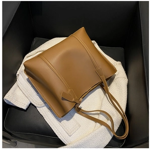 Detail view of large brown faux leather tote bag placed on a white tweed jacket