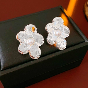 Close-up of silver irregular flower earrings with pearls on black leather background