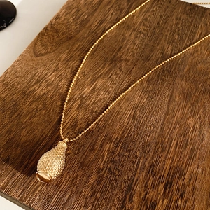 Macro shot of gold textured teardrop pendant with bead chain on dark wood background