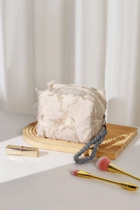 Detail of linen makeup bag with frayed fringe texture and checkered wristlet strap