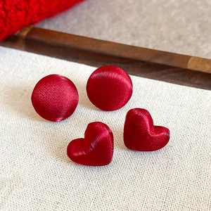 Dettaglio dei orecchini a perno in raso rosso tondi e a cuore con texture setosa