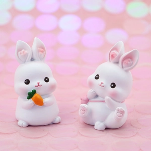 Close-up of cute white resin rabbit figurines with carrot and pink bag on pink background