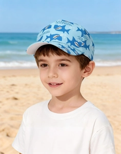 Détail d'une casquette enfant bleue avec imprimé requin portée par un garçon à la plage
