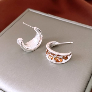 Macro view of C-shaped silver earrings with leopard print enamel detail on jewelry box
