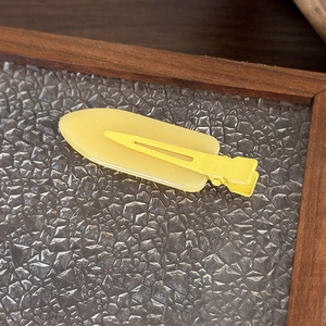 Dettaglio di un fermaglio per capelli in resina gialla opaca su vetro e legno